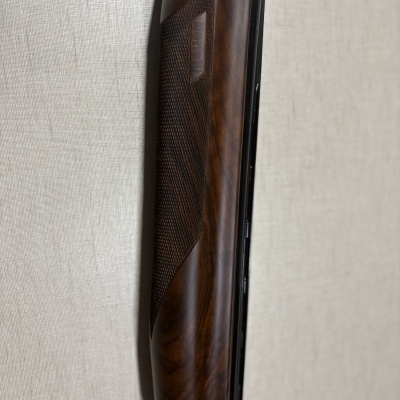 Parte da espingarda com cano preto e empunhadura em madeira castanha com textura xadrez