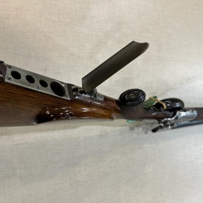 Espingarda antiga de madeira e metal com tampa aberta sobre fundo claro