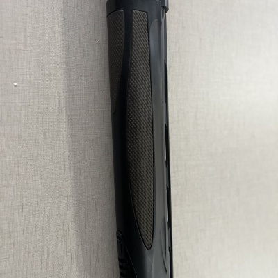 Parte de uma arma de fogo preta com detalhes texturizados sobre superfície cinza