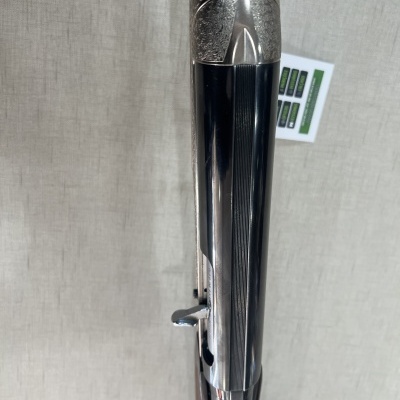 Espingarda metálica com detalhes gravados e partes pretas sobre fundo bege