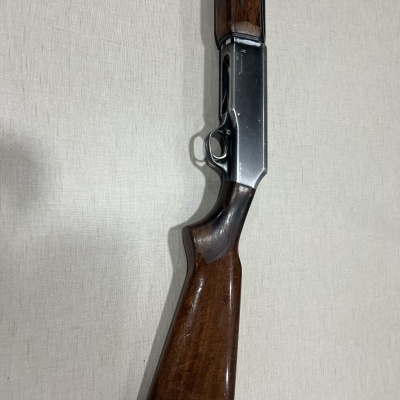 Rifle com madeira castanha e metal prateado, contra fundo claro