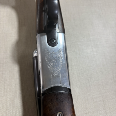 Espingarda com corpo em madeira escura e metal prateado decorado com gravações detalhadas.