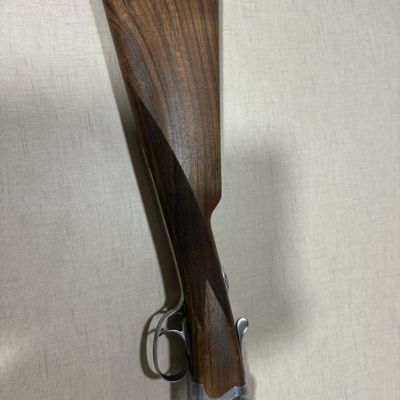 Parte traseira e gatilho de espingarda com coronha em madeira castanha e detalhes metálicos