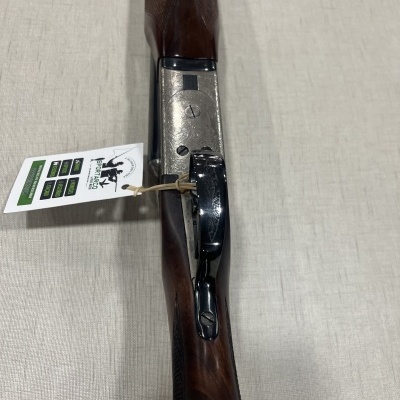 Espingarda com cabo de madeira castanha e detalhes metálicos prateados e pretos, com etiqueta pendurada