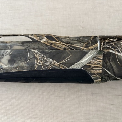 Arma de caça Beretta camuflada com padrão de folhagem em cinza, castanho e preto e texto no cano.