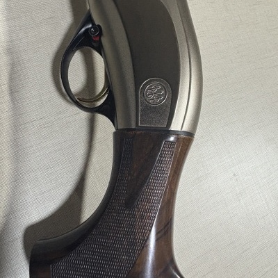 Pega de espingarda em madeira castanha com corpo metálico cinzento e gatilho preto