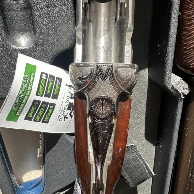 Espingarda de cano duplo com acabamento em madeira e aço decorado dentro de mala acolchoada.