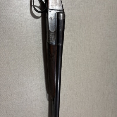 Espingarda de caça dupla em madeira e metal encostada a uma parede bege