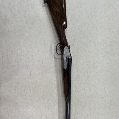 Espingarda de canos paralelos com madeira escura e metal escuro em fundo claro