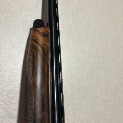 Parte de arma de fogo com coronha de madeira castanha e cano preto sobre fundo claro