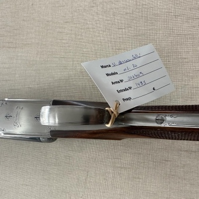 Espingarda prateada com detalhes em madeira escura e etiqueta branca com informações manuscritas