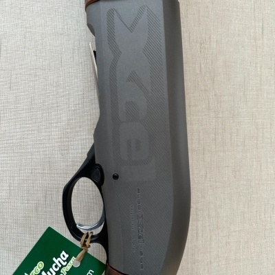 Espingarda de caça com partes em madeira castanha e corpo em metal cinza escuro com etiqueta verde e branca