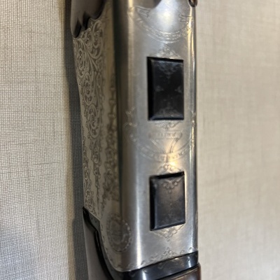 Espingarda com detalhes em metal gravado e madeira escura sobre fundo de tecido claro