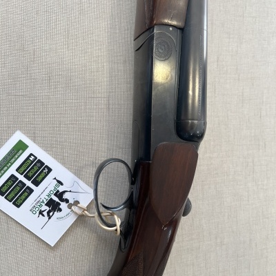 Espingarda de canos paralelos com madeira escura e canos pretos, com etiqueta branca