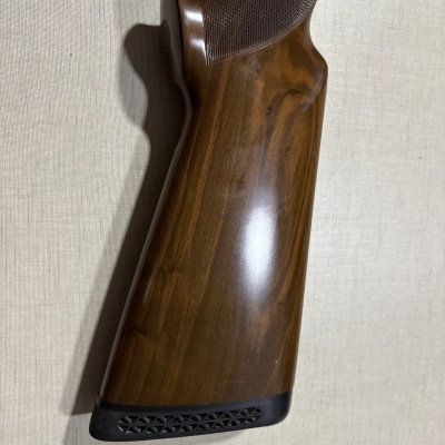 Coronha de arma em madeira polida com ponteira preta numa superfície clara.