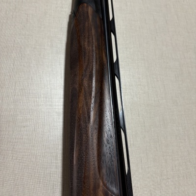 Ponteira de arma de fogo com punho em madeira castanha texturada e metal cinza e preto