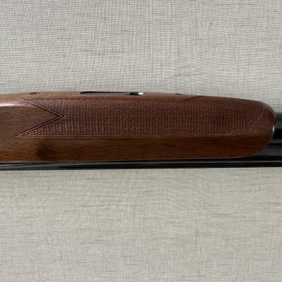 Parte de uma arma de fogo com madeira castanha e metal prateado sobre tecido cinzento