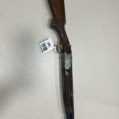 Espingarda de caça com madeira escura e metal preto pendurada numa parede cinzenta