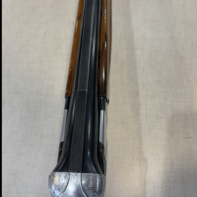 Espingarda dupla com coronha em madeira e armação metálica gravada vista de cima.