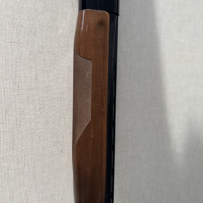 Parte de uma espingarda com punho de madeira castanha e corpo metálico preto