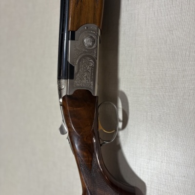 Espingarda com madeira escura e metal prateado gravado, sobre tecido claro