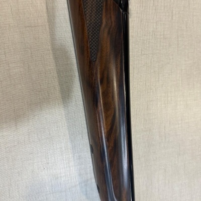 Coronha de espingarda em madeira escura com textura quadriculada e parte metálica preta