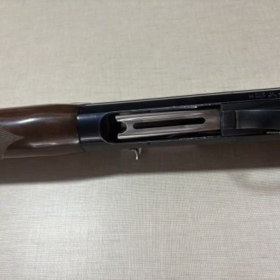 Espingarda com coronha de madeira castanha e parte metálica preta e prateada em fundo claro