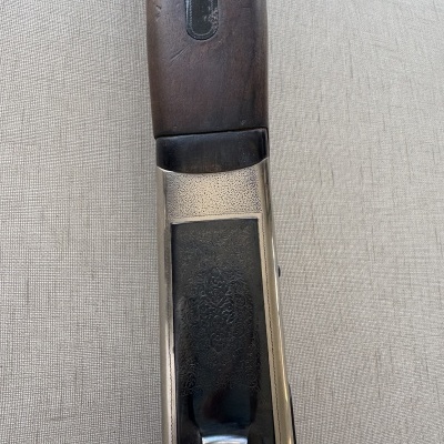 Empunhadura de arma com madeira escura e metal gravado