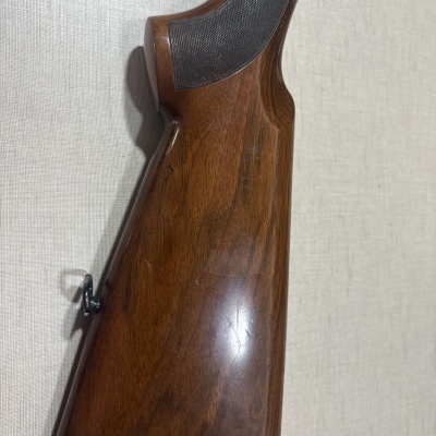 Coronha de arma em madeira castanha com textura preta e presilha metálica.