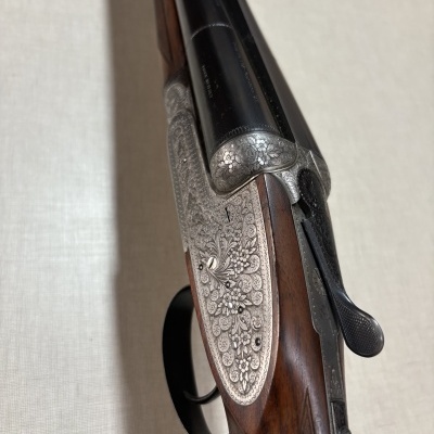 Espingarda com cabo de madeira escura e gravações florais em metal