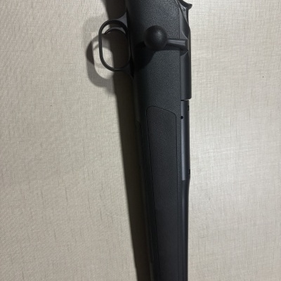 Detalhe da parte central de uma arma de fogo preta sobre fundo claro.
