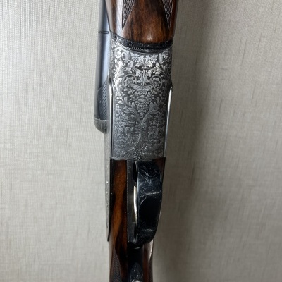 Espingarda de madeira e metal com gravações decorativas encostada em parede clara