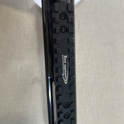 Trilho de montagem preto com parafusos e texto branco em objeto metálico preto sobre superfície clara