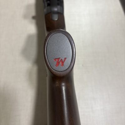 Coronha de espingarda em madeira castanha com placa metálica cinza e letra vermelha W