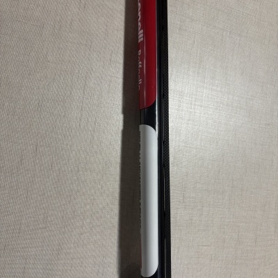 Objeto cilíndrico preto com etiqueta vermelha e branca e texto visível em tecido claro.