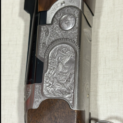 Espingarda com cabo em madeira e corpo metálico gravado sobre superfície clara.