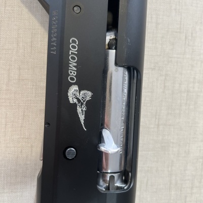 Parte de espingarda metálica preta com cabo de madeira castanha e texto COLOMBO