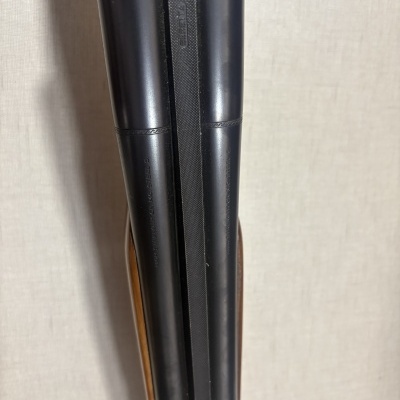 Duas coronhas metálicas pretas com detalhes gravados e texto em relevo, com partes em madeira castanha ao lado, sobre fundo bege texturizado.