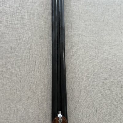 Espingarda de canos duplos com punho em madeira e detalhes metálicos sobre tecido cinzento