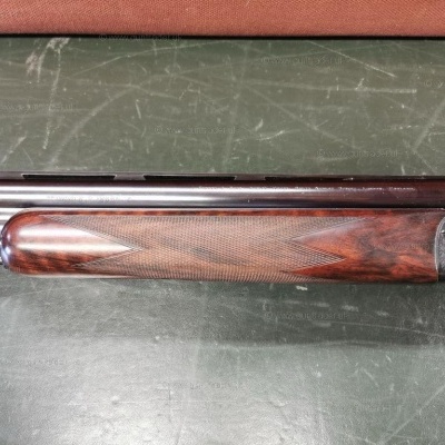 Espingarda com madeira entalhada e canos negros sobre superfície verde desgastada