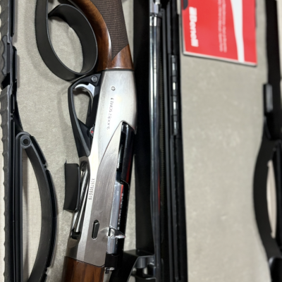 Espingarda de caça com coronha em madeira castanha e partes metálicas prateadas numa caixa acolchoada.