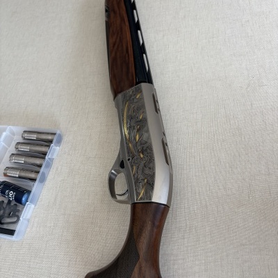 Espingarda com detalhes em madeira, metal prateado gravado e caixa com cartuchos e óleo para armas.