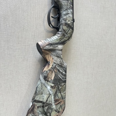 Espingarda camuflada com gatilho preto encostada a uma parede cinzenta