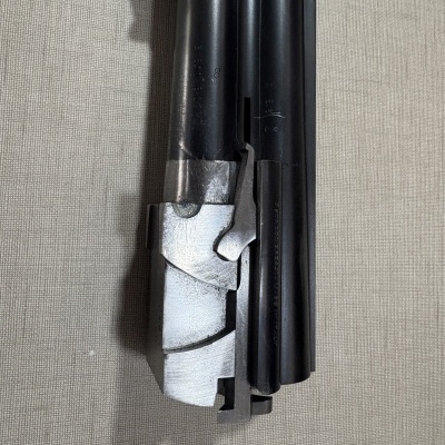 Parte frontal de uma arma de fogo metálica em preto e prateado sobre tecido cinzento.