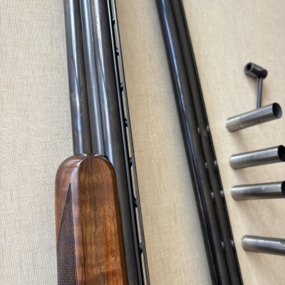 Arma de fogo de cano duplo com madeira castanha e metal preto e três canos metálicos adicionais.
