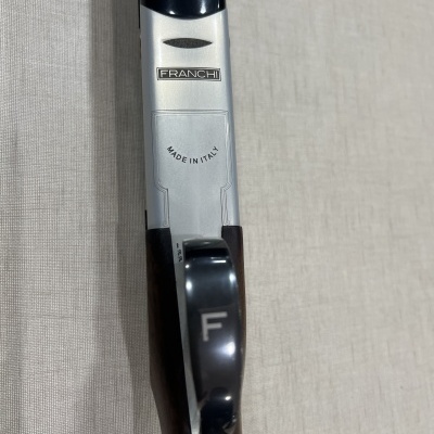 Detalhe do corpo de uma espingarda em madeira e metal com inscrições FRANCHI e MADE IN ITALY.