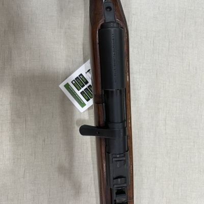 Espingarda com cabo em madeira castanha e metal preto sobre tecido claro com documento ao lado