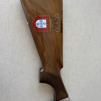 Parte traseira de espingarda com madeira polida, metal gravado e brasão de armas colorido