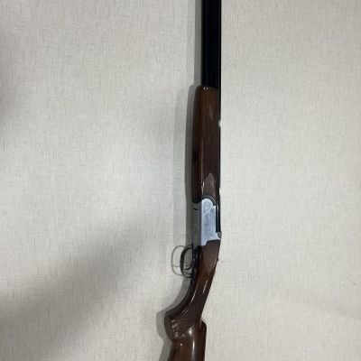 Espingarda de canos duplos com madeira castanha e canos pretos encostada a parede clara