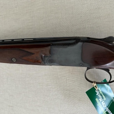 Espingarda de cano duplo com madeira castanha e metal cinza escuro, etiqueta verde pendurada